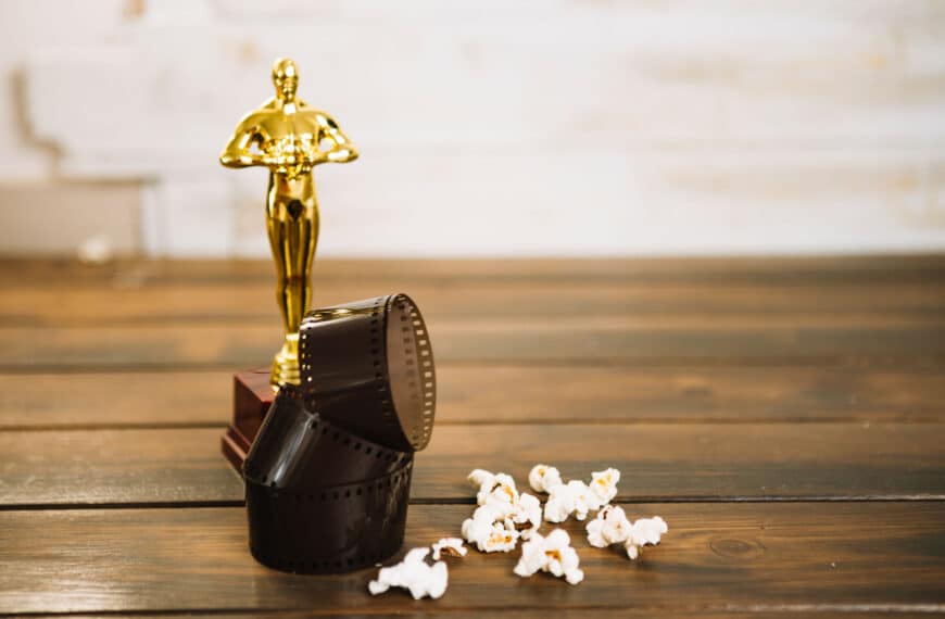 Drehort - Eine Trophäe, die einer Preisstatue ähnelt, neben einer umgestürzten Filmrolle mit losen Filmstreifen und Popcorn auf einer Holzoberfläche, symbolisiert die Top 3 christlicher Filme.